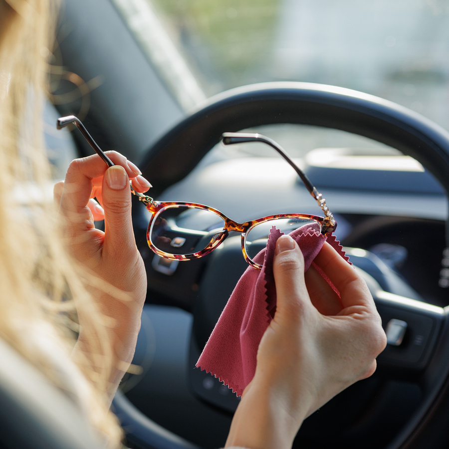 close up of woman wiping glasses in car, ensuring clear vision before driving.